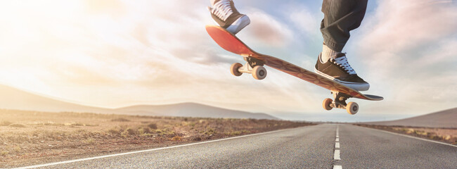 Young skateboarder guy jumping and performing a trick on the a desert road asphalt isolated on sky...