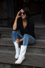 Young beautiful woman in white leather boots, sitting on wooden stairs and smiling