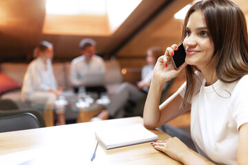 Beautiful young confident woman at loft style office with group of colleagues in background. Concept of success, business, career, achievements