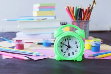 Alarm clock on the table, against the background of multi-colored paper, books and stationery, back to school, education, table for schoolchildren