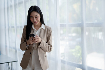 Fototapeta premium Beautiful Asian businesswoman using smartphone to check work contact customers, answer chats, complete transactions and use social media applications various in the office.