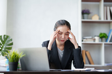 Beautiful Asian businesswoman is tired from working in the office. because of using too much eyes while working on laptop computer in office.