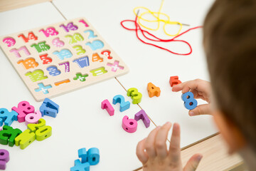 kid learning numbers through game. Sensory activity with wooden numbers and shoe laces. Educations at home, pre-school education, Montessori methodology. sequence of numbers, arithmetic problems.