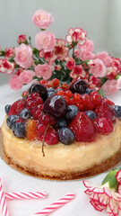 Berry birthday cake. Cheesecake with cherries, raspberries, currants and blueberries. Cake, pink candles and red flowers on a white background. Photo for stories.