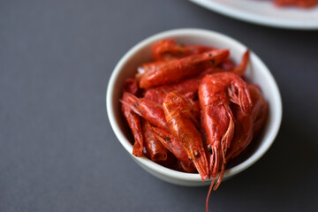 A delicious appetizer of red shrimp with spices. Peppered shrimp in a salad bowl on a black background. Spicy seafood appetizer.