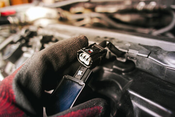 The auto mechanic is unplugging the ignition coil of the car engine in the engine compartment.