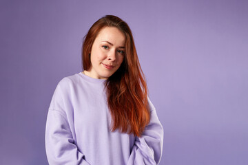 Fototapeta premium Caucasian woman in violet sweatshirt. Natural look. Smiling. long red hair. Violet background
