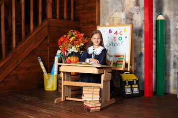 Portrait of a school girl on lesson in classroom. Back to school. A cute hardworking child is sitting at table in of chalkboard in school. Kid is studying in classroom against background of blackboard