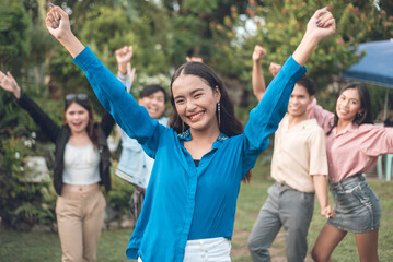 A pretty young woman celebrating in front with her friends. Raising her hands in success and victory. Teamwork concept.