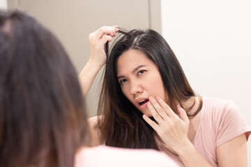 Asian beautiful woman look herself through mirror and pull her hair and touch her lip with worry about hair loss and grey hair.