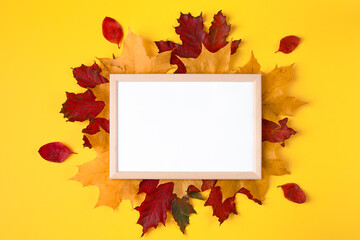 Naklejka na ściany i meble Empty wooden frame mock up and autumn leaves on yellow background. Template for design.
