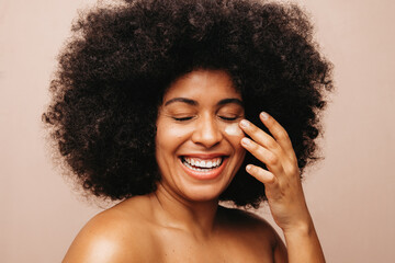 Happy young woman applying moisturizing cream on her face