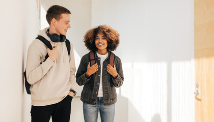 Smiling friends walking in college corridor. Classmates talking to each other.