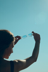 silhouette of a woman holding sunglasses against the blue sky