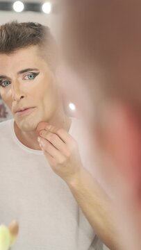Drag queen looking into the mirror while applying make-up on face with a makeup sponge. Lgbt concept.