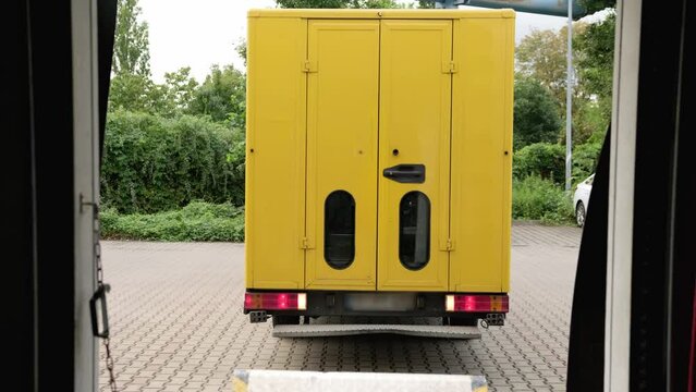 A yellow delivery van reverses and parks to load the truck with parcels