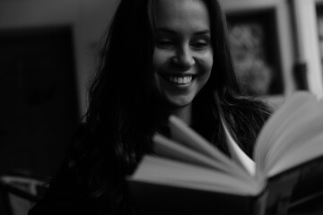 Black and white portrait of a young brunette girl with a book in her hands. Women is siting in the chair 