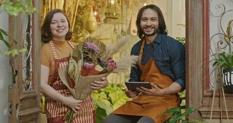 One employee of flower shop smiling at camera holding bouquet of beautiful flowers arrangement. A joyous female local business employee standing inside store