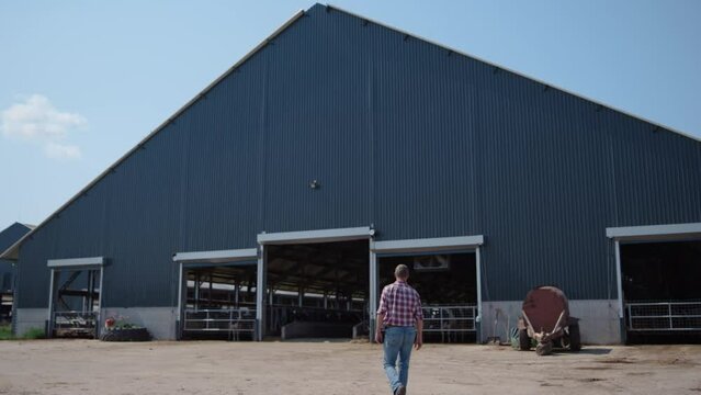 Farmer going modern barn producing organic food. Specialist walking to farm.