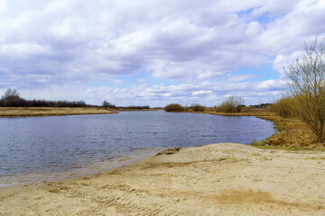 River with cloudy skies and willows growing along the shore in spring or early summer. Cloudy sky