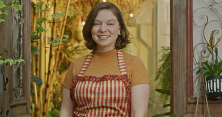 Fototapeta premium Happy employee wearing apron smiling at camera. Portrait of a young female worker of small business