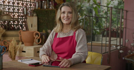 Portrait of owner of small business. Businesswoman wearing apron owner of flower shop smiling at camera inside store. A middle aged female entrepreneur smiling at camera