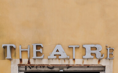 An old rusty sign saying 'theatre' on a yellow wall above the entrance. Abstract background or symbol picture for theaters. Theatre sign in vintage lettering, font style. 