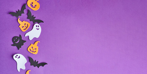Halloween decorations, pumpkins, candy, on purple background. Halloween party greeting card. Copy space. Flat lay, top view, overhead.