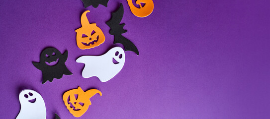 Halloween decorations, pumpkins, candy, on purple background. Halloween party greeting card. Copy space. Flat lay, top view, overhead.