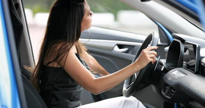 Businesswoman driver prepares for driving on road getting in car. Woman in black top fastens seat belt looking with concerned and serious expression