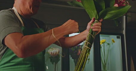 A small business employee of flower shop creating a bouquet of flowers arraignment. An Asian...