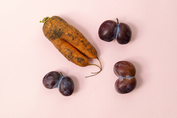 Ugly plums and carrot on pink background. fruits are suitable for food. Concept Reduction of...
