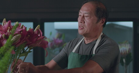 Fototapeta premium An Asian American florist preparing bouquet of flowers for online delivery. Portrait of an artisan male florist creating artistic arrangement for client at flower shop