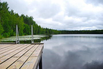 Forest lake. Trees surround the lake. Wooden bridge with handrails on the lake. The mirror surface of the water. Rustic landscape. Landscapes of Russia