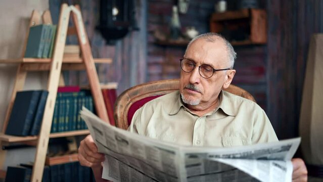 Confident elderly man reading daily newspaper interesting information sitting on vintage armchair 