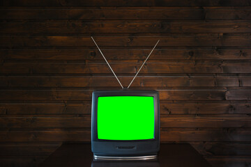 Old analoque retro tv with isolate green screen mock up on dark brown wooden background on table in living room. 90's style