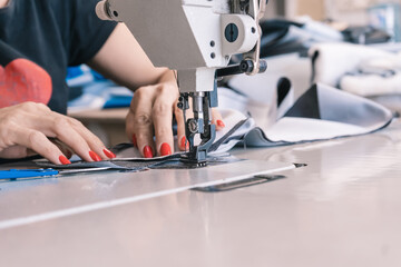 The seamstress sews at the sewing machine, threads the fabric. Women's hands