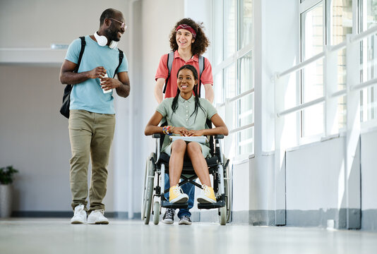 Group of students walking along school corridor after lesson together with their friend with disability