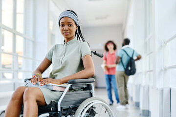 Portrait of African teenage girl sitting in wheelchair and looking at camera during break at school