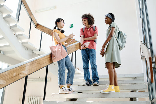 Group of teenagers talking to each other after lessons while standing on stairs of school building