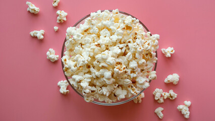 A glass transparent bowl full of popcorn on a pink background