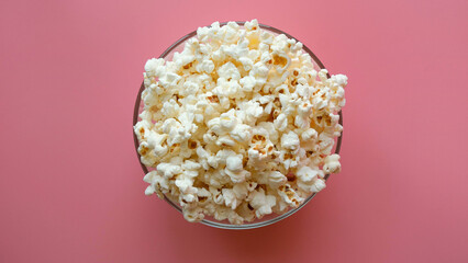 A glass transparent bowl full of popcorn on a pink background