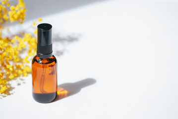 Amber pump bottle with serum, tonic or essential oil with yellow flowers. White background with daylight. Beauty concept for face and body care