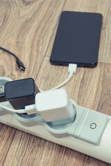 Black smartphone and chargers connected to electrical power strip. Various devices charging concept