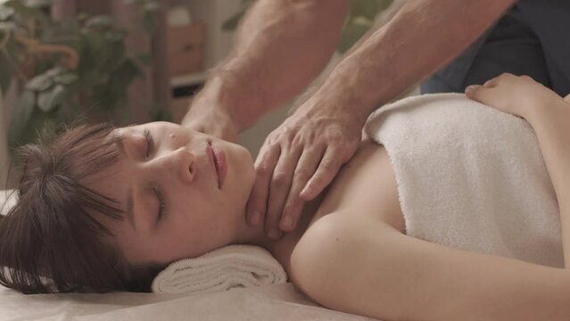 Slowmo of beautiful young woman enjoying neck massage done by professional masseur in spa salon