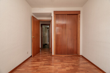 Empty bedroom with bright reddish parquet, matching fitted wardrobes with sliding doors, white gotelet painted walls and cloakroom to the rear