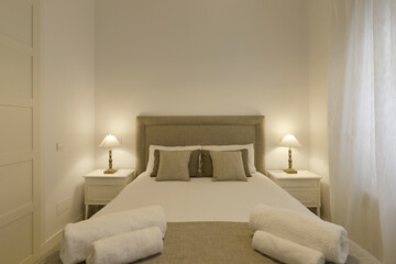 Double bedroom with gray upholstered fabric headboard, matching cushions and two twin lamps on bedside tables with drawers