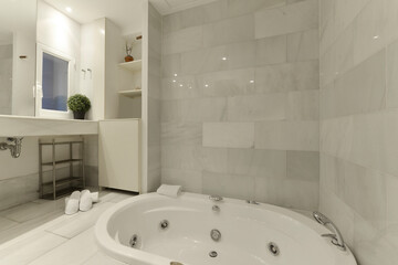 Hydromassage bathtub in a bathroom with white marble tiling and a large countertop with matching sink