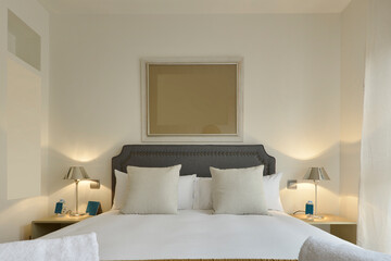 Fototapeta na wymiar Bedroom with headboard upholstered in blue fabric, pillows and cushions and twin chrome metal lamps