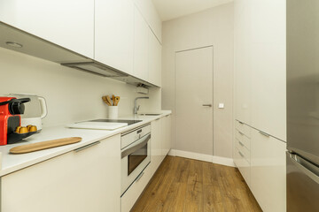 Small kitchen with white furniture and matching appliances with chestnut flooring